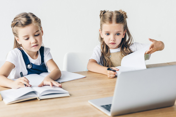 маленькие школьницы, занимающиеся с ноутбуком на рабочем столе изолированы на белом
 - Фото, изображение