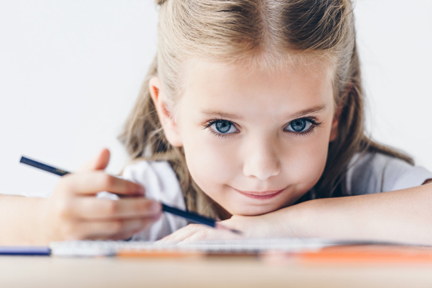 close-up portrait of little schoolgirl drawing with color pencils and looking at camera isolated on white - Photo, Image