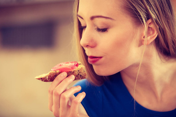 Sağlıklı kahvaltı yapan genç bir kadın mutfakta lezzetli sandviçler yiyor. İyi diyet konsepti. - Fotoğraf, Görsel
