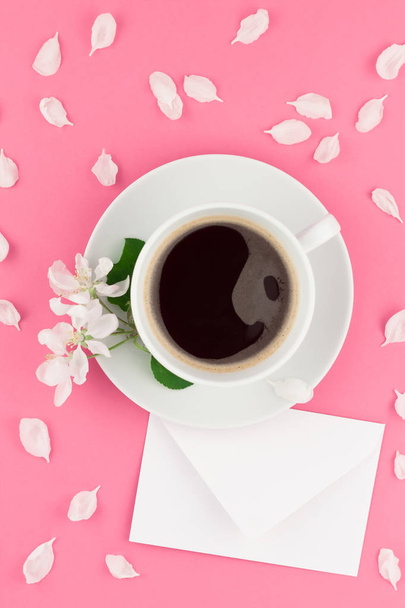 Creative flat lay concept top view of coffee cup and white apple tree flowers petals on pastel pink background with postcard mock up and copy space in minimal style, template for text - Foto, Bild
