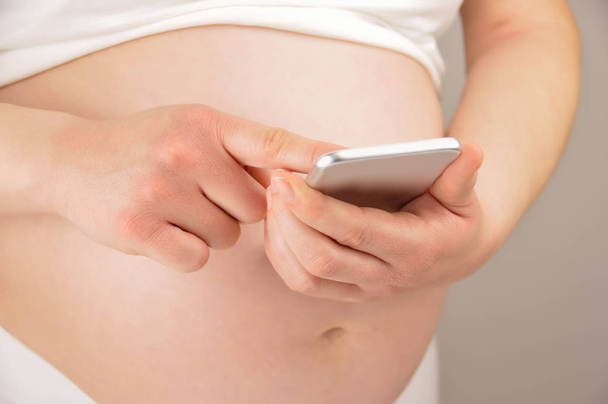 a pregnant woman using a cellphone against a white background - Foto, Bild