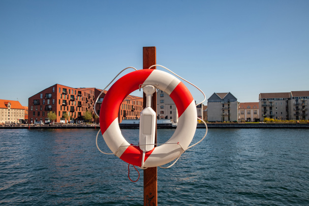 Закрыть вид на плывущее кольцо с городской рекой и зданиями на заднем плане в Коппеле, Дания
 - Фото, изображение