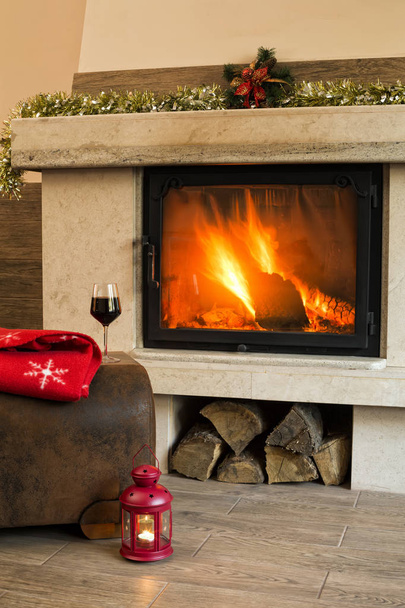 Weihnachtlicher Hintergrund mit brennender Kerze, Glas Rotwein und roter Decke vor dem weihnachtlich dekorierten Kamin - Foto, Bild