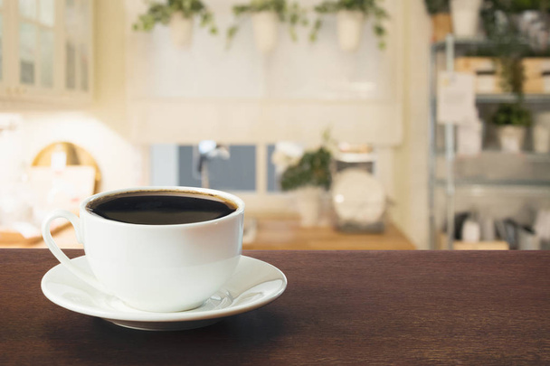 Kopje zwarte koffie op houten tafelblad in wazig moderne keuken of een café. Close-up. Binnenshuis. - Foto, afbeelding