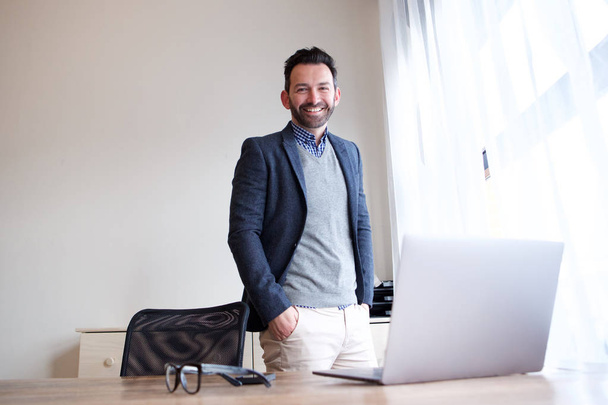 Porträt eines selbstbewussten Geschäftsmannes, der mit Laptop im Büro lächelt - Foto, Bild
