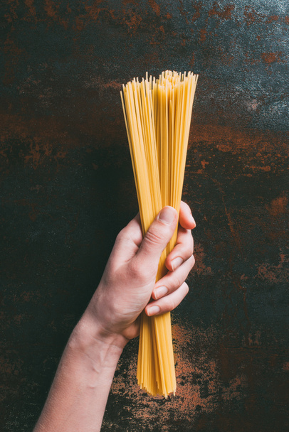 cropped image of man holding raw spaghetti over rustic metal tabletop  - Foto, Imagem