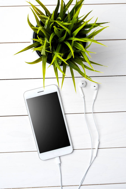 Modern smartphone with earphones on white wooden background - Foto, Bild