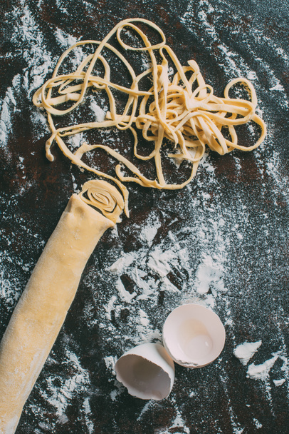 top view of dough, egg shell and raw pasta on table covered by flour  - Valokuva, kuva