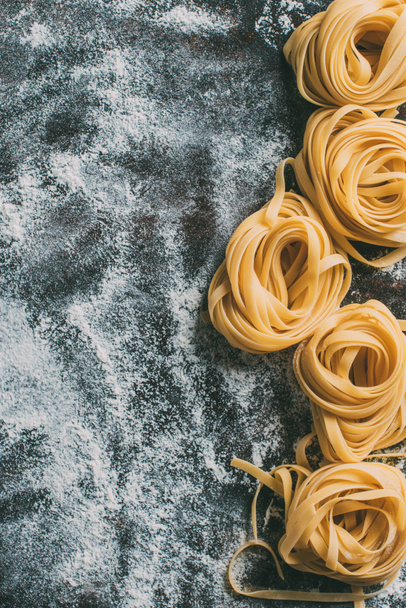 top view of raw tagliatelle pasta on table covered by flour  - Photo, Image