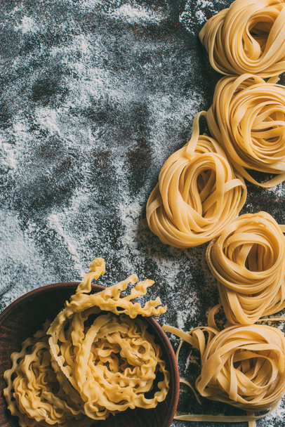 top view of raw pasta in bowl and on table covered by flour - Photo, image