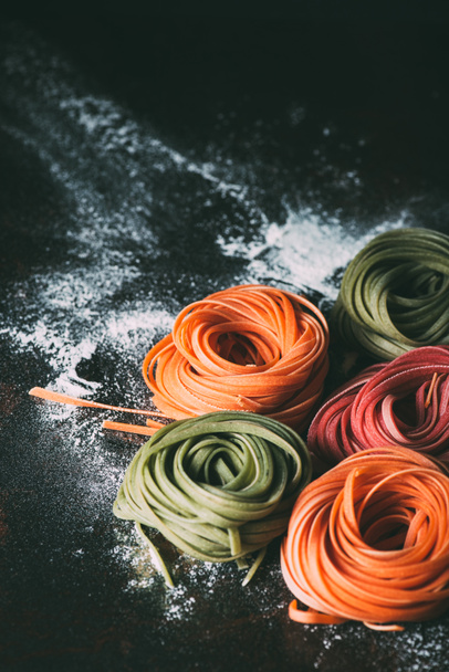 Close-up weergave van ruwe kleurrijke tagliatelle pasta op tafel gedekt door bloem  - Foto, afbeelding
