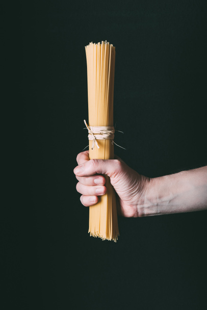 cropped image of holding spaghetti wrapped by ribbon isolated on black background  - Zdjęcie, obraz