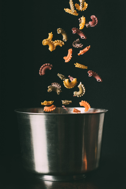 closeup shot of colorful pasta falling into pan on black background  - Foto, Imagen
