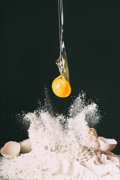 close up view of yolk falling on flour on black background  - 写真・画像