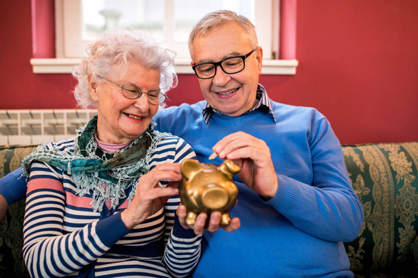 Senior paar zet munt aan piggy bank, sparen geld voor pensioen - Foto, afbeelding