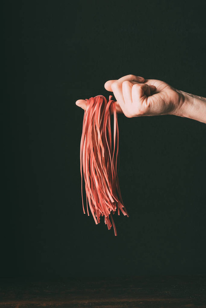 cropped image of man holding raw red tagliatelle on finger over table on black background  - Фото, изображение