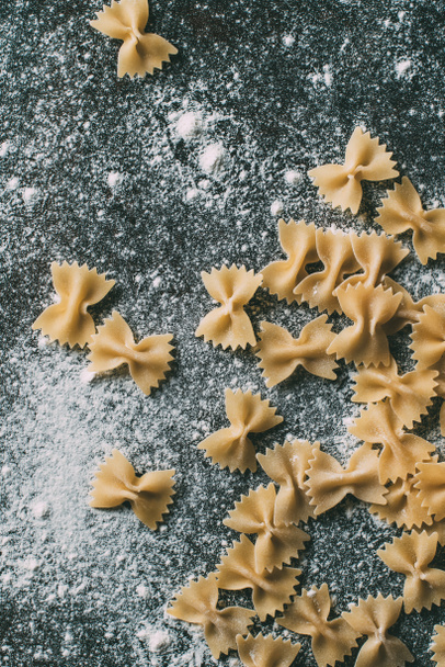 top view of raw farfalle pasta on table covered by flour  - Foto, Imagem