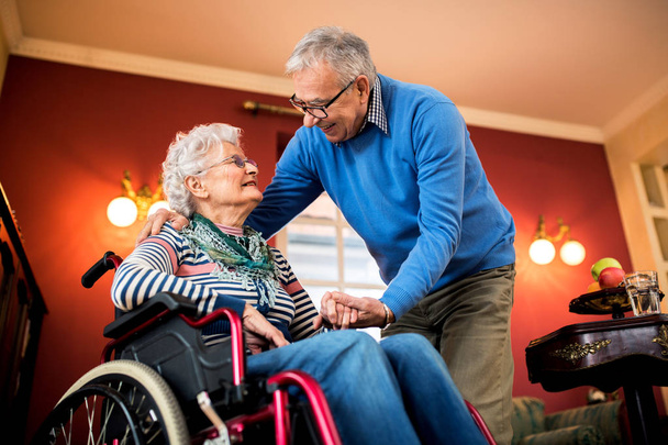 Senior paar verliefd, senior mens verzorgen van zijn vrouw in rolstoel - Foto, afbeelding