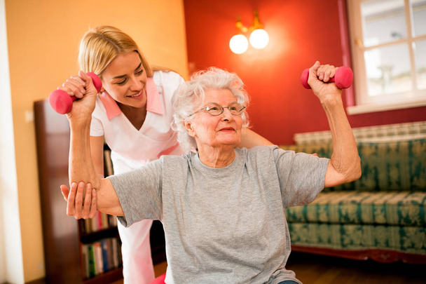 Smilinig positif femme âgée profiter en exercice avec infirmière tout en tenant haltères
 - Photo, image