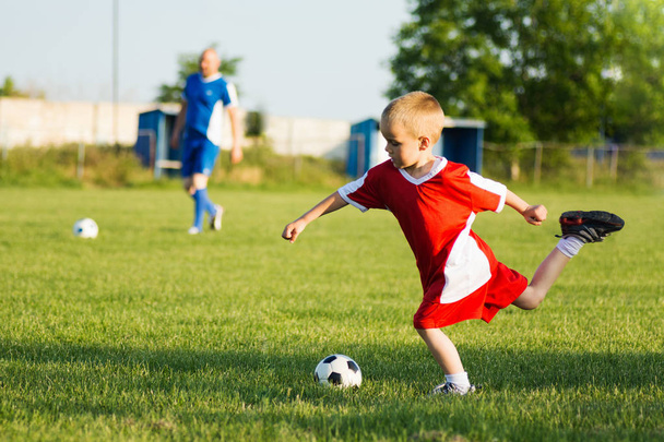Der 4-jährige Junge schießt den Fußball beim Fußballtraining im Freien auf dem Spielfeld. - Foto, Bild