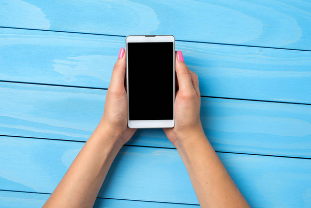 Жінка використовує білий смартфон над синім дерев'яним столом
 - Фото, зображення