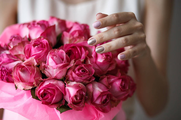 Close-up photo of gorgeous bouquet of pink roses in a hat box. Woman hands with manicure, nail polish art - Photo, Image