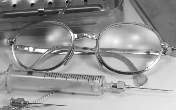 Seringa velha em vidro frágil com agulha de aço e os óculos antigos do médico com efeito preto e branco
 - Foto, Imagem