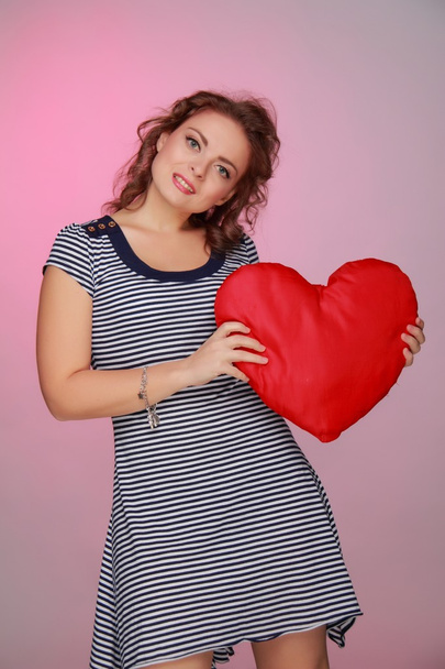 Beautiful woman in a striped dress holding a big heart - Foto, afbeelding