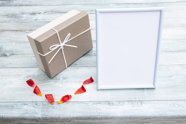Caja de regalo con un marco de imagen blanca con lugar para su texto y hojas de tulipán en la mesa rústica de madera brillante. Concepto de tarjeta
.  - Foto, imagen