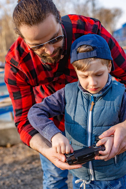 Father and son holding remote control joystick and piloting quadrocopter. Close up - 写真・画像