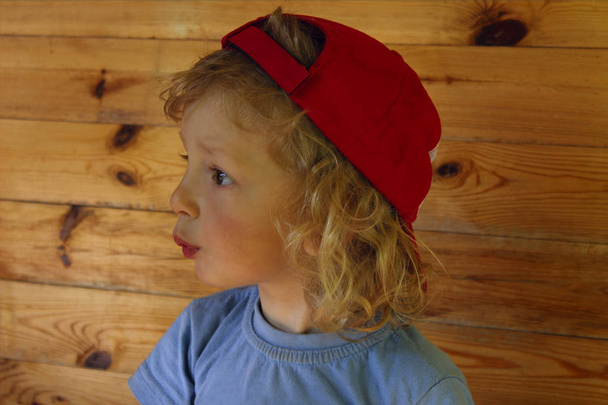 Вырезанный снимок милого маленького мальчика с вьющимися волосами в красной шляпе и смотрящего в сторону. Веселый мальчик
. - Фото, изображение