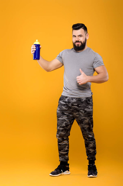 Handsome strong man drinks water on yellow background - Valokuva, kuva