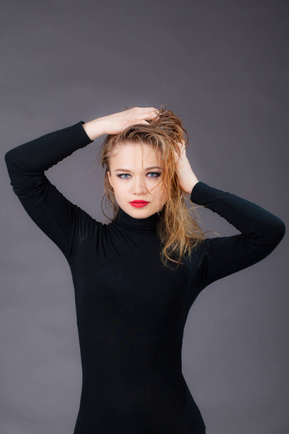 Portrait of a girl in black clothes, holding her hands wet hair. Studio shot, on a gray background - Foto, imagen
