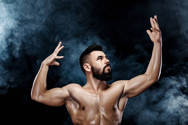 Handsome strong bodybuilder posing in studio on smoke background - Foto, Imagen