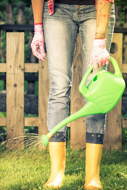 Getatoeëerde vrouw watring planten in de tuin dragen kaplaarzen. - Foto, afbeelding