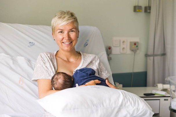 Mãe amamentando seu bebê recém-nascido menino em uma cama de hospital
 - Foto, Imagem
