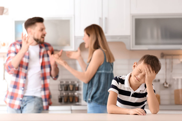 Little unhappy boy sitting at table while parents arguing on kitchen - Photo, Image