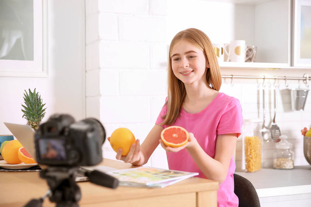 Cute teenage blogger with fruits recording video at table - Фото, изображение