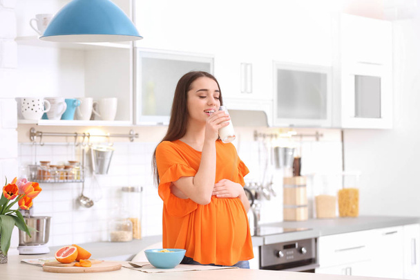 Beautiful pregnant woman drinking milk in kitchen - Фото, зображення