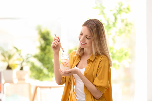 Молодая привлекательная женщина ест вкусный йогурт в помещении
 - Фото, изображение