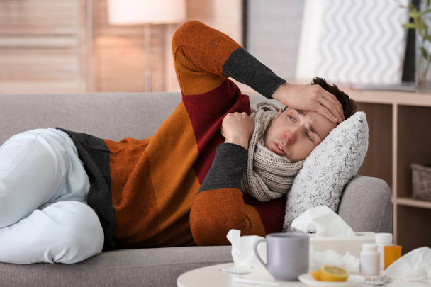 Sick young man with headache suffering from cold on sofa at home - Valokuva, kuva