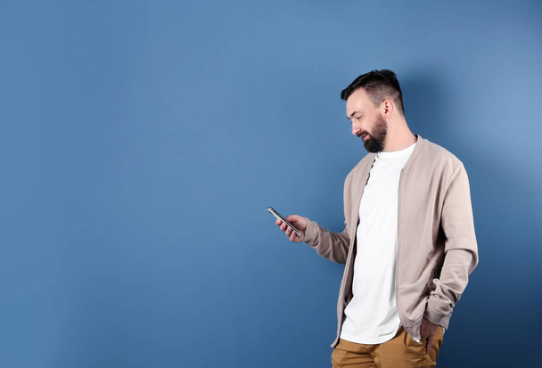 Portrait of handsome bearded man with mobile phone on color background - 写真・画像