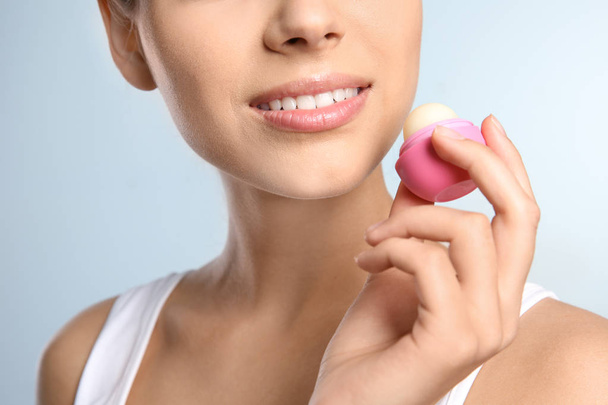 Young woman applying balm on her lips against color background, closeup - Foto, afbeelding