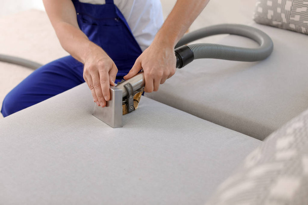 Dry cleaning worker removing dirt from sofa indoors - 写真・画像