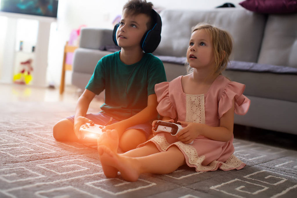 Little brother and sister playing video games lying on the couch - Photo, Image