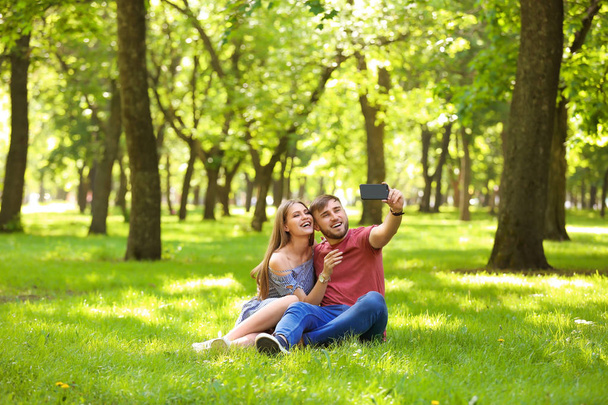 Happy young couple taking selfie on green grass in park - Фото, изображение
