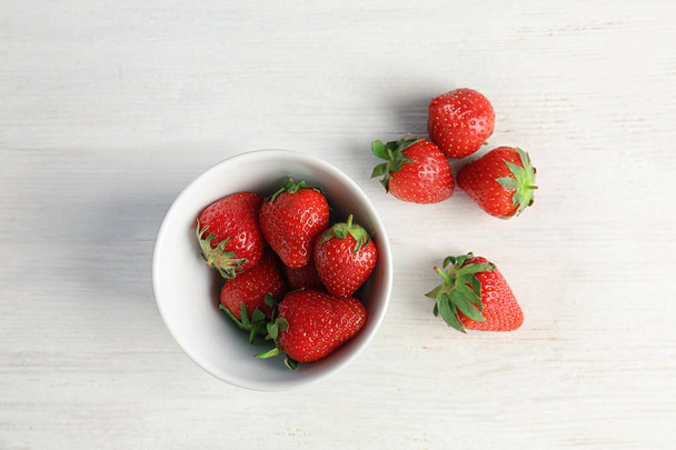Ripe red strawberries and bowl on light background, top view - Foto, Bild