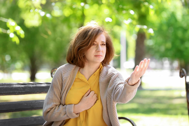 Mature woman having heart attack on bench in park - Photo, Image