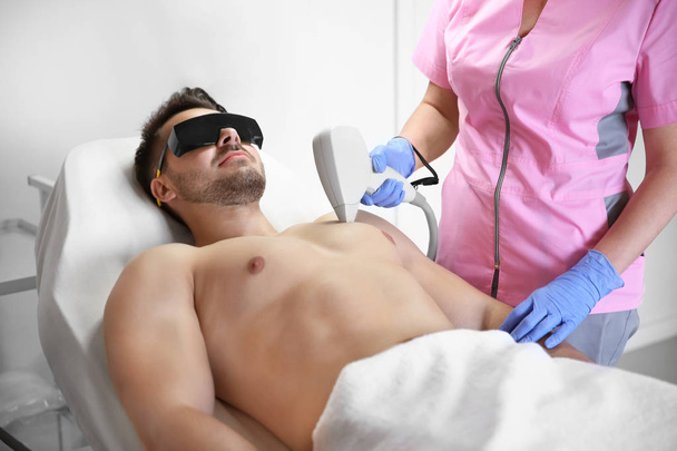Young man undergoing laser epilation procedure in beauty salon - Fotó, kép