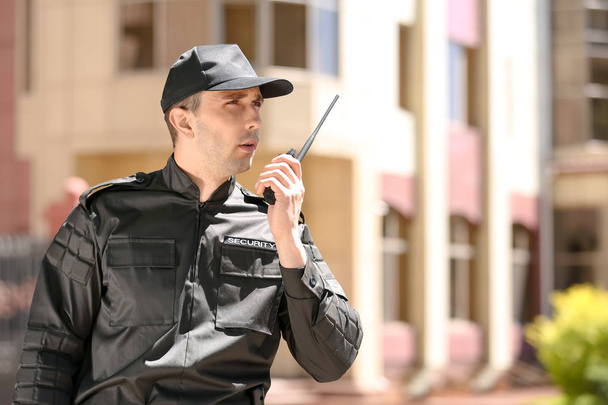 Male security guard using portable radio transmitter outdoors - Foto, afbeelding